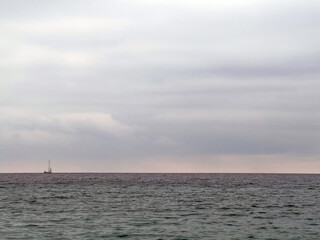 Obraz premium Solitary sailboat on tranquil ocean under overcast sky