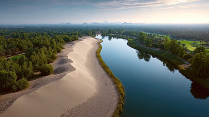 Desert sand meets lush green forest along winding river, tranquil landscape with clear sky and distant mountains