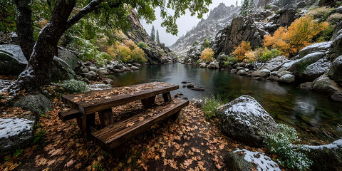 Peaceful mountain river scene with a wooden picnic table, autumn leaves, and a dusting of snow, capturing the quiet beauty of a changing season in a serene forest landscape.
