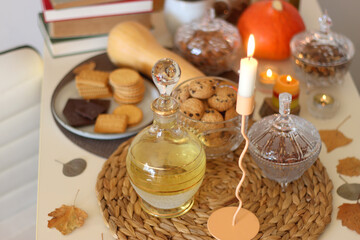 Lit candles, cookies, chocolate, nuts, tea, wine, pumpkins, books, reading glasses and autumn leaves on the table. Autumnal hygge at home. Selective focus.