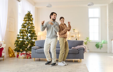 Fun dance of Christmas couple at home, smiling man and woman enjoy music in cozy living room by...
