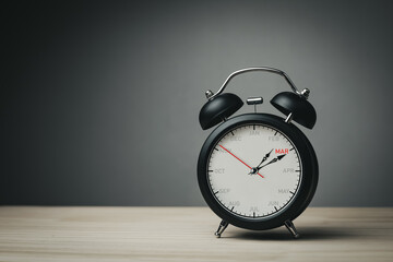 The hands of clock point to March on dial black alarm clock with copy space. Concept of monthly goal planning, important appointments and effective time management.