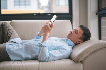 Portrait of asian man lying on a couch or sofa while using smart phone in living room