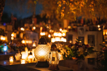 Night scenes from the cemetery in Zielonki during All Saints Day. Warm candlelight, golden autumn trees, glowing lanterns and peaceful atmosphere with visitors walking along the paths.