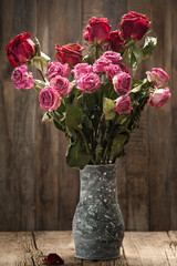 Bouquet of dry roses in a clay vase on a wooden background. Unhappy love, loneliness, sadness, old age, loss.