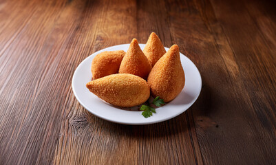 A plate of Brazilian coxinha snacks, on a wooden table. Typical snack food from Brazil made from shredded chicken and deep fried.