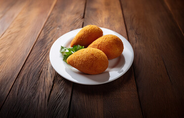 Coxinha made from shredded chicken coated with breadcrumbs. Typical Brazilian snack food, on a white plate on wooden table. Often sold as street food.