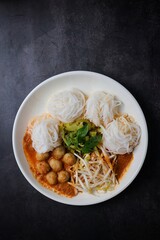 Kanomjeen namya krati ,Rice vermicelli with minced fishes ,Chicken feet,meatballs and coconut milk in red curry on ceramic plate side dish with vegetables
