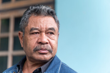 Fototapeta premium A candid outdoor portrait of a thoughtful senior Asian man. He has a pensive expression, wearing a denim jacket.