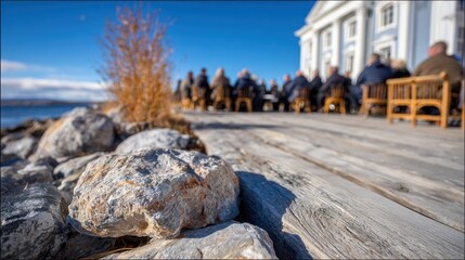 Scenic lakeside meeting: Rocks frame gathering on a wooden deck with a blue sky backdrop, fostering connection amidst nature's serenity.