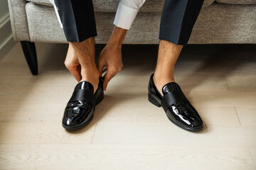 Close-up of a groom putting on polished black patent loafers before a wedding. Elegant, minimalist composition capturing sophistication, preparation, and modern masculine style
