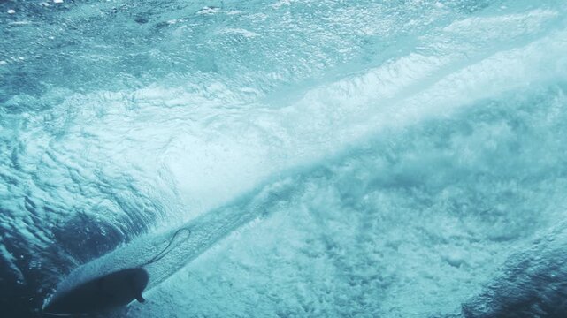 Minimalist silhouette of board and leash outline against white foam from barreling wave, underwater rearview slow motion