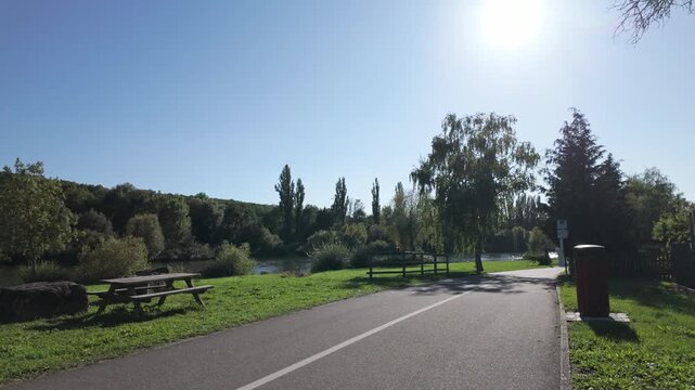The famous 600 km long River Main Cycleway and a calm park area with green grass, trees and some benches next to the River Main in Frickenhausen am Main. Sunny summer afternoon in Bavaria - Germany.