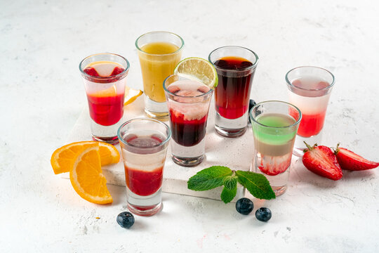 Various alcoholic drinks in glasses on a white table, mixed shots of berries and oranges