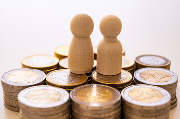 Wooden figures, symbolizing a man and a woman, placed on coins, symbolize the connection between feelings, material stability, and the economic aspects of the couple.