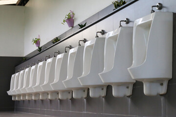  Neatly arranged toilet bowls for men, tiled floor, hygienic restroom interior, symmetrical layout.