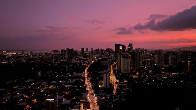 Aerial view of illuminated city buildings under the colorful dusk sky, showcasing the contrast between the artificial lights and the fading daylight, Cebu City, Central Visayas, Philippines.