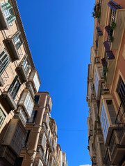 A view of a narrow street from below, with ornate facades and balconies. Spain, 2022.