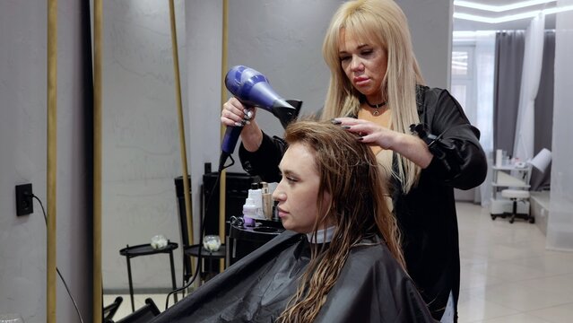 Experienced stylist blow drying customer's hair in a contemporary salon, offering professional hair styling services