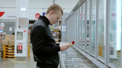 Shopper examines product labels while comparing various frozen food options in the supermarket's...