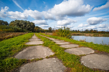 Autumn riverside path with stepping stones and colorful foliage under a cloudy sky in Małopolska, Poland.