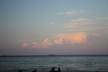 Calm sea horizon with ships and pink clouds at sunset