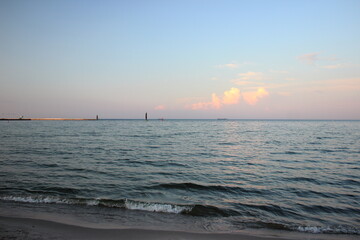 Calm sea horizon with ships and pink clouds at sunset