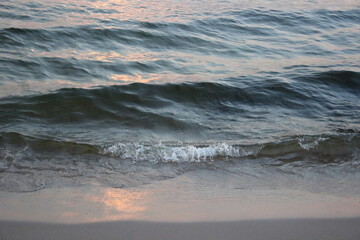 Sea wave washing sandy beach at sunset