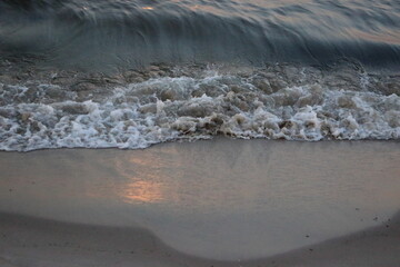 Sea wave washing sandy beach at sunset