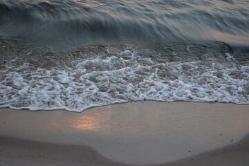 Sea wave washing sandy beach at sunset