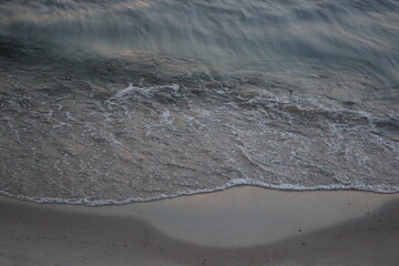Sea wave washing sandy beach at sunset