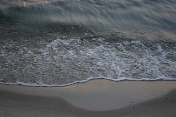 Sea wave washing sandy beach at sunset