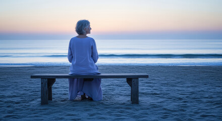 Senior woman sitting on a wooden bench on a sandy beach, looking at the ocean during sunset