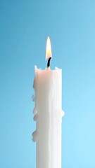 Lit candle with dripping wax against a light blue background