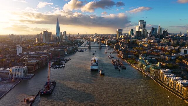 Panoramic aerial view of the skyline of London, United Kingdom, along the Thames river with boat traffic and Tower Bridge during golden sunset time