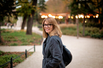 Stylish middle-aged woman walking in the city park in an autumn day