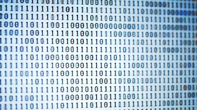 Closeup of a computer screen displaying a continuous stream of binary code representing digital data programming and the abstract concept of information technology in a modern hightech environment.