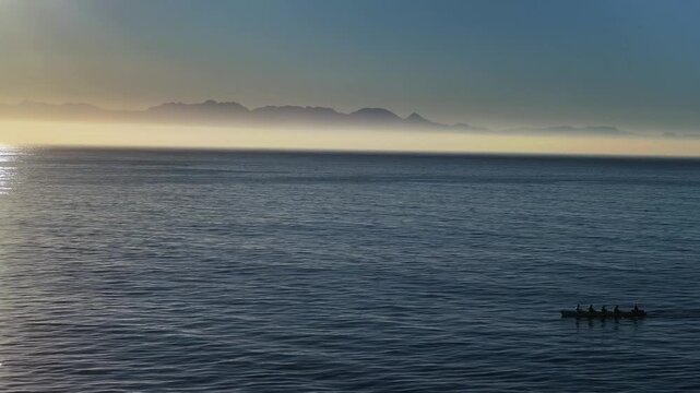 Aerial view of a rowboat cutting across the tranquil, deep blue sea, with the iconic Table Mountain shrouded in a soft, ethereal mist, Cape Town, Western Cape, South Africa.