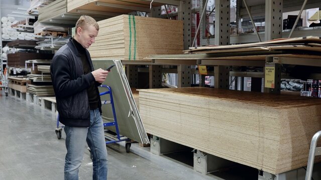 Construction worker uses smartphone to compare prices and check inventory in lumber department of hardware store. translator: good price