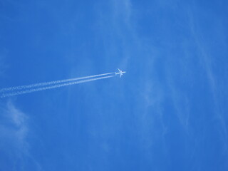 Airplane from below with two white contrails against blue sky. Minimal composition.