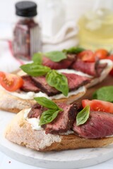 Delicious bruschettas with roast beef served on white table, closeup