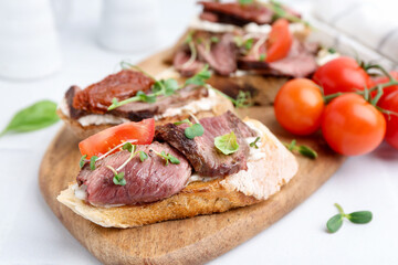 Delicious bruschettas with roast beef served on white table, closeup