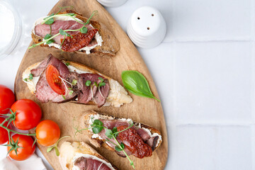 Delicious bruschettas with roast beef served on white tiled table, flat lay. Space for text