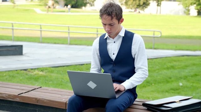 Young man works on laptop outside, greenery, focus, business vibe