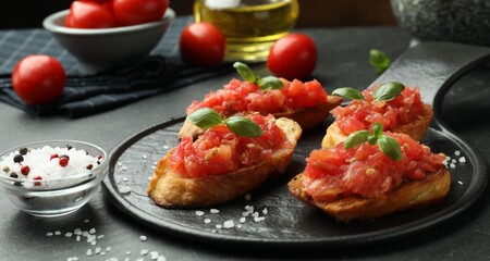 Tasty bruschettas with tomatoes and basil served on black table, closeup