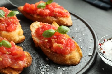 Tasty bruschettas with tomatoes and basil served on black table, closeup