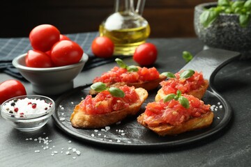 Tasty bruschettas with tomatoes and basil served on black table, closeup