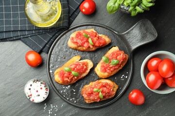 Tasty bruschettas with tomatoes and basil served on black table, flat lay