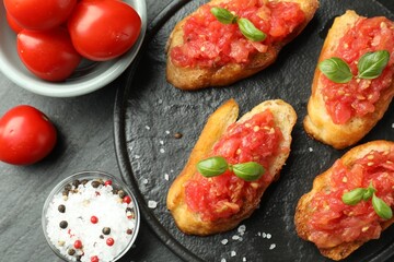 Tasty bruschettas with tomatoes and basil served on black table, flat lay