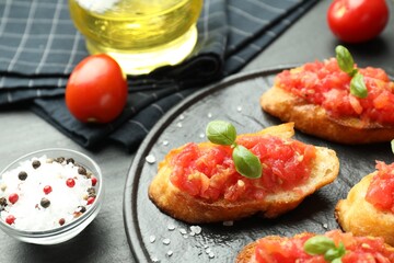 Tasty bruschettas with tomatoes and basil served on black table, closeup